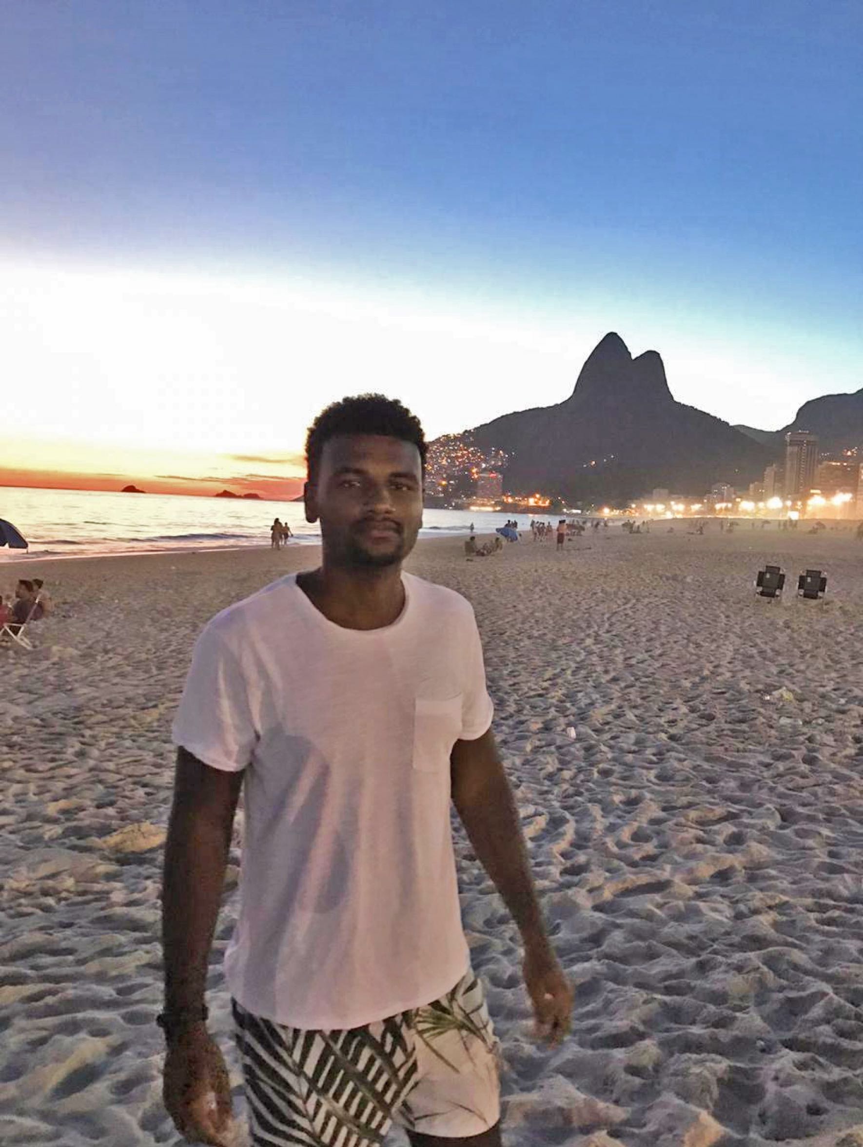 Das Bild zeigt Matheus bei Sonnenuntergang am Strand in Rio de Janeiro. Im Hintergrund sind die Lichter der Stadt zu sehen.