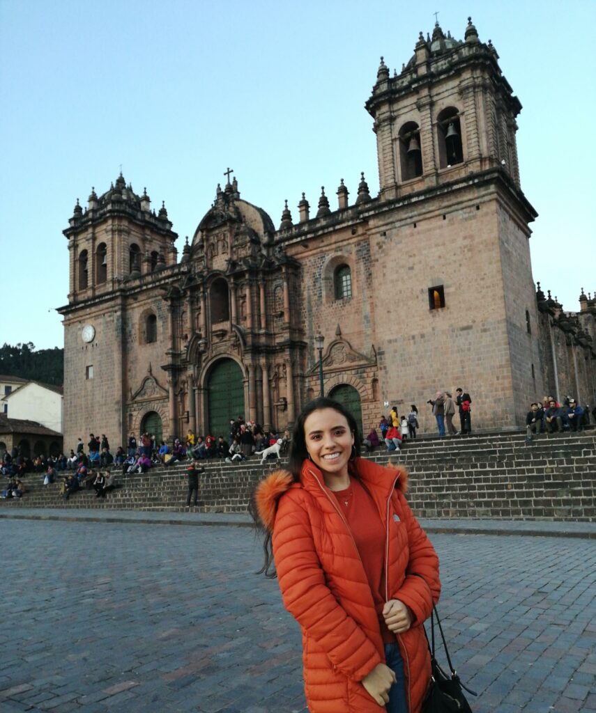 Auf dem Bild ist Liza in einem orangefarbenen Mantel zu sehen zu sehen, wie sie auf dem Plaza de Armas in Santiago de Chile vor der Kathedrale steht.