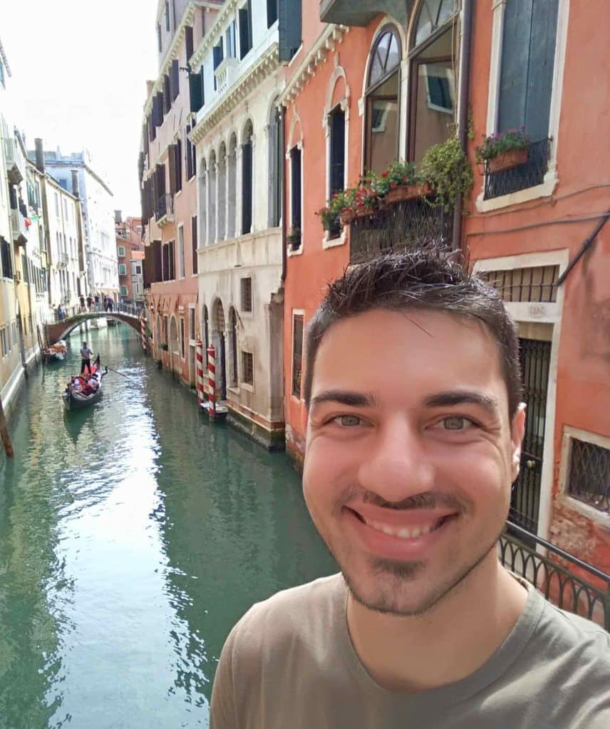 Orestis smiling broadly, in the background a Venetian canal with old house facades and a gondolier.