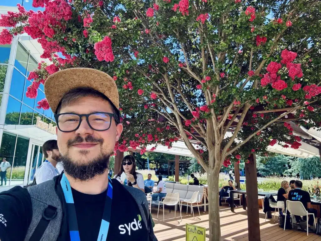 Danny standing in an outdoor seating area in front of a tree with pink blossom