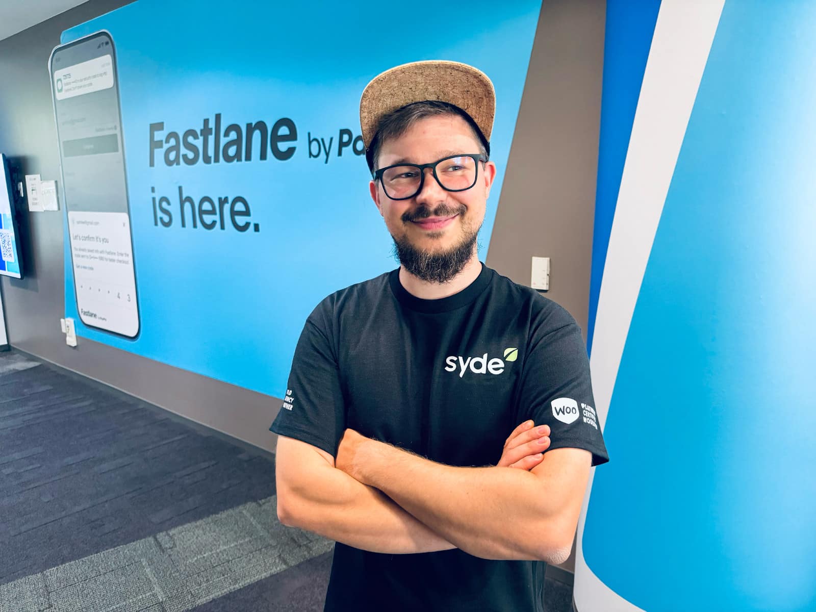 Danny posing arms crossed and smiling in front of a banner wall stating "Fastlane by PayPal is there.